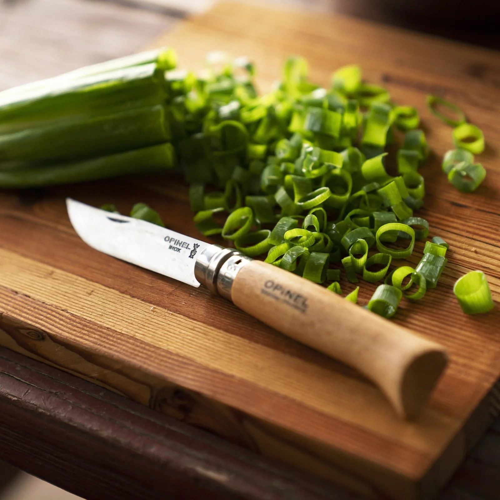Opinel knife and scallions on a wooden cutting board